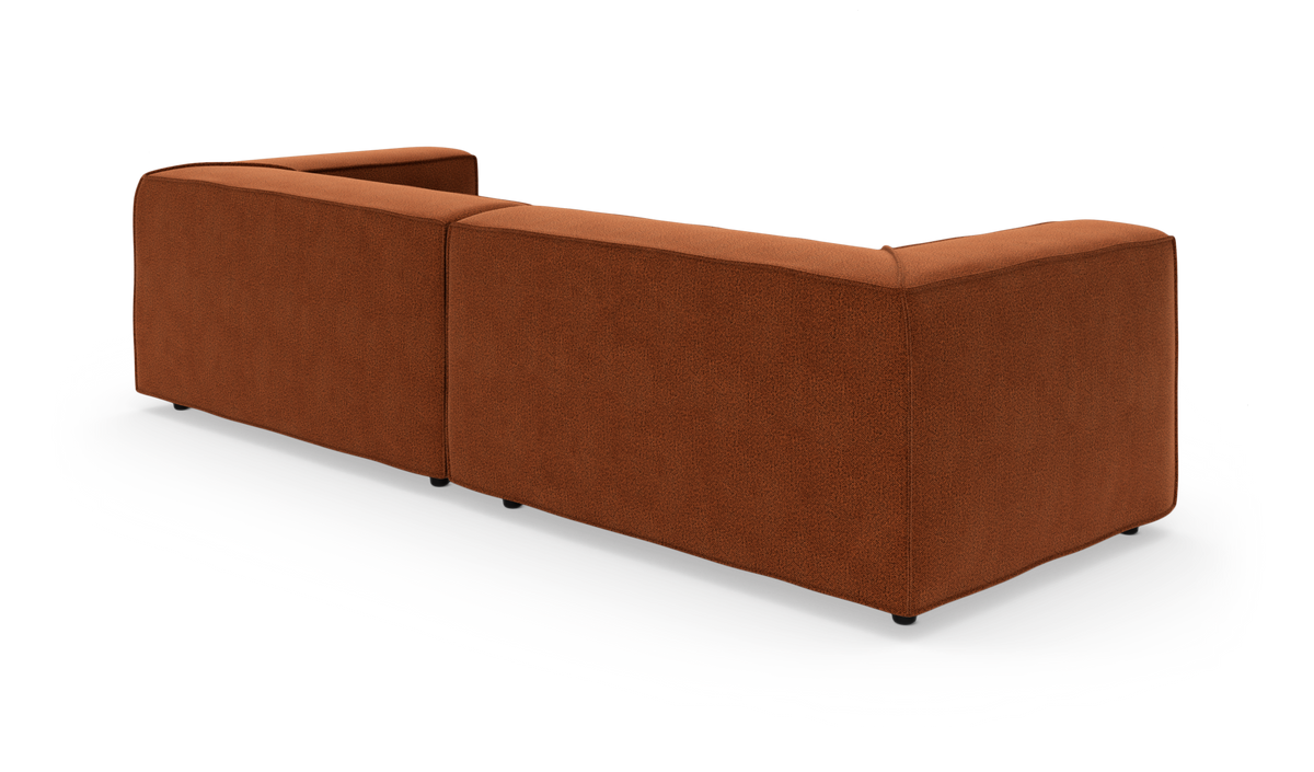Modulsofa i rostrødt stof set skråt bagfra, isoleret på hvid studiobaggrund.