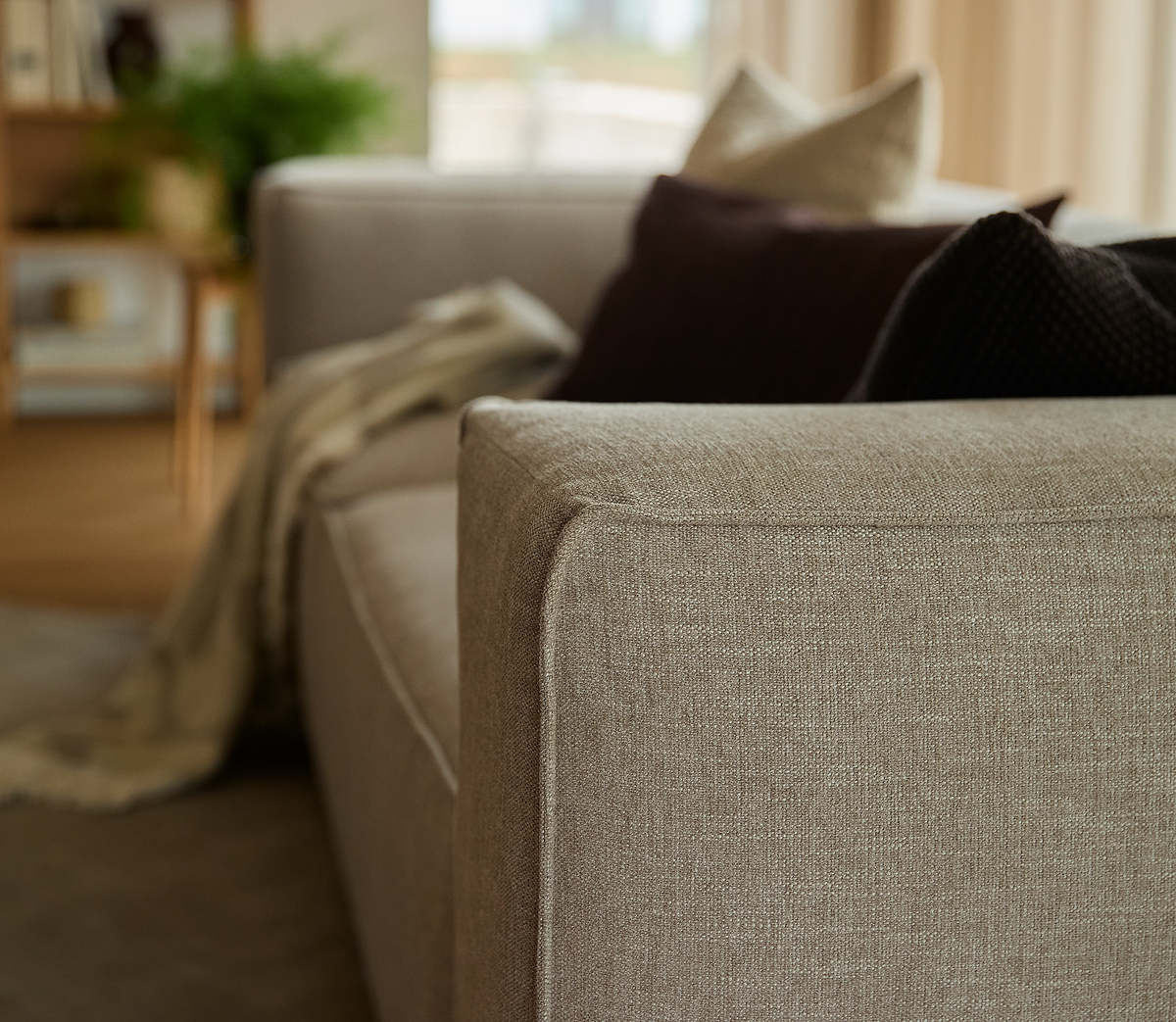 Nærbillede af en beige stofsofa med puder og en plaid i en lys stue.