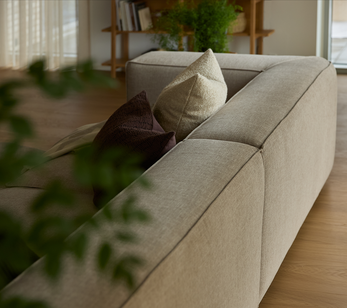 Beige modulsofa med puder i neutrale toner, grønne planter og trædetaljer i en lys stue.