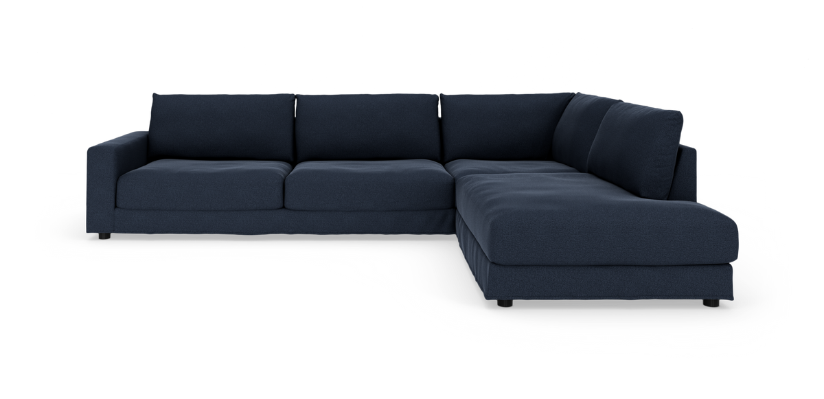 Mørkeblå L‑sofa i stof med bred chaiselong, frontvinkel i studiemiljø.