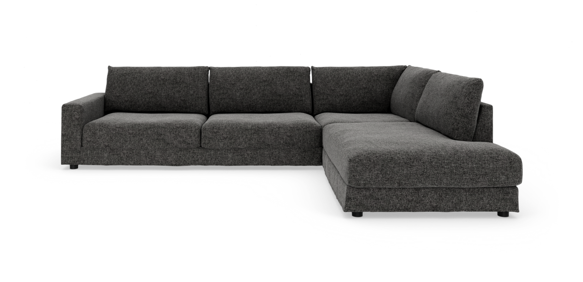 Mørkegrå L‑sofa med chaiselong til højre, bløde hynder og brede armlæn.