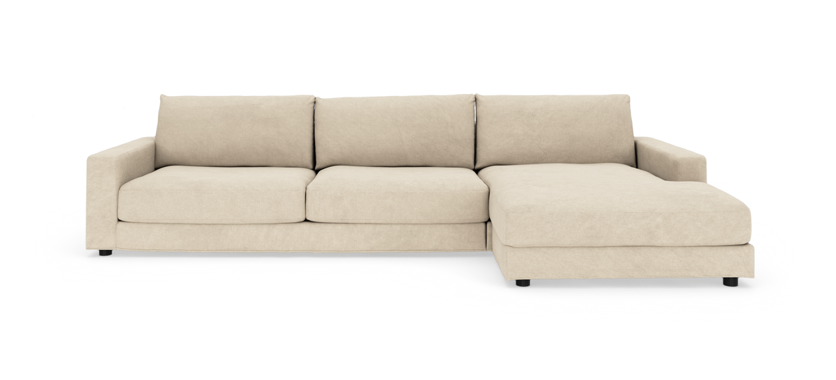 Beige hjørnesofa med chaiselong til højre, bløde ryghynder og lav, moderne profil, frilagt på hvid baggrund.