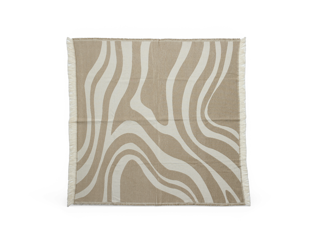 Beige og offwhite plaid/tæppe med bølget, organisk mønster og frynsede kanter.