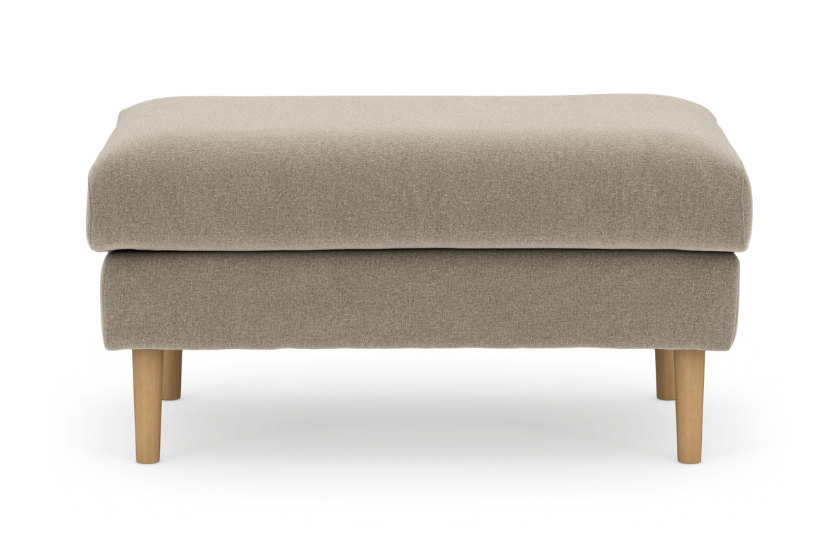 Beige polstret ottoman/fodskammel med runde træben, set lige forfra mod hvid baggrund.