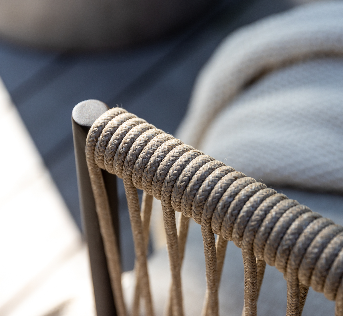 Nærbillede af flettet rebdetalje på en beige udendørsstol med metalstel i dagslys.