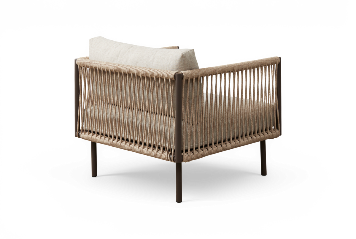 Beige loungestol i flettet reb med lyse hynder og slanke metalben, set skråt bagfra.