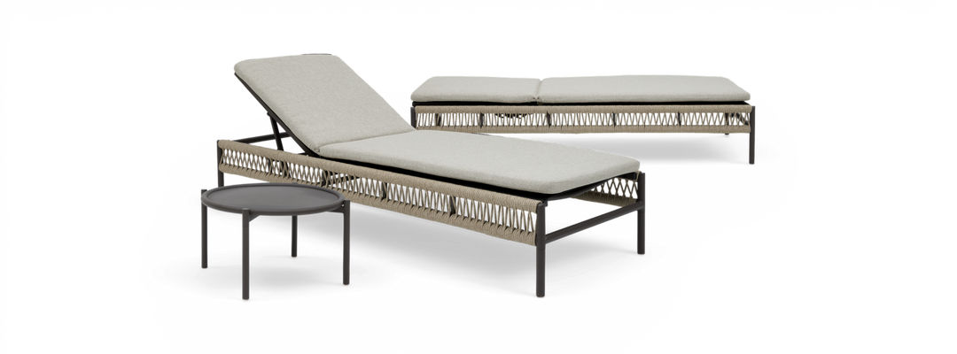 To solsenge i flettet rebdesign med lyse hynder og et lille rundt sidebord, frilagt på sort baggrund.