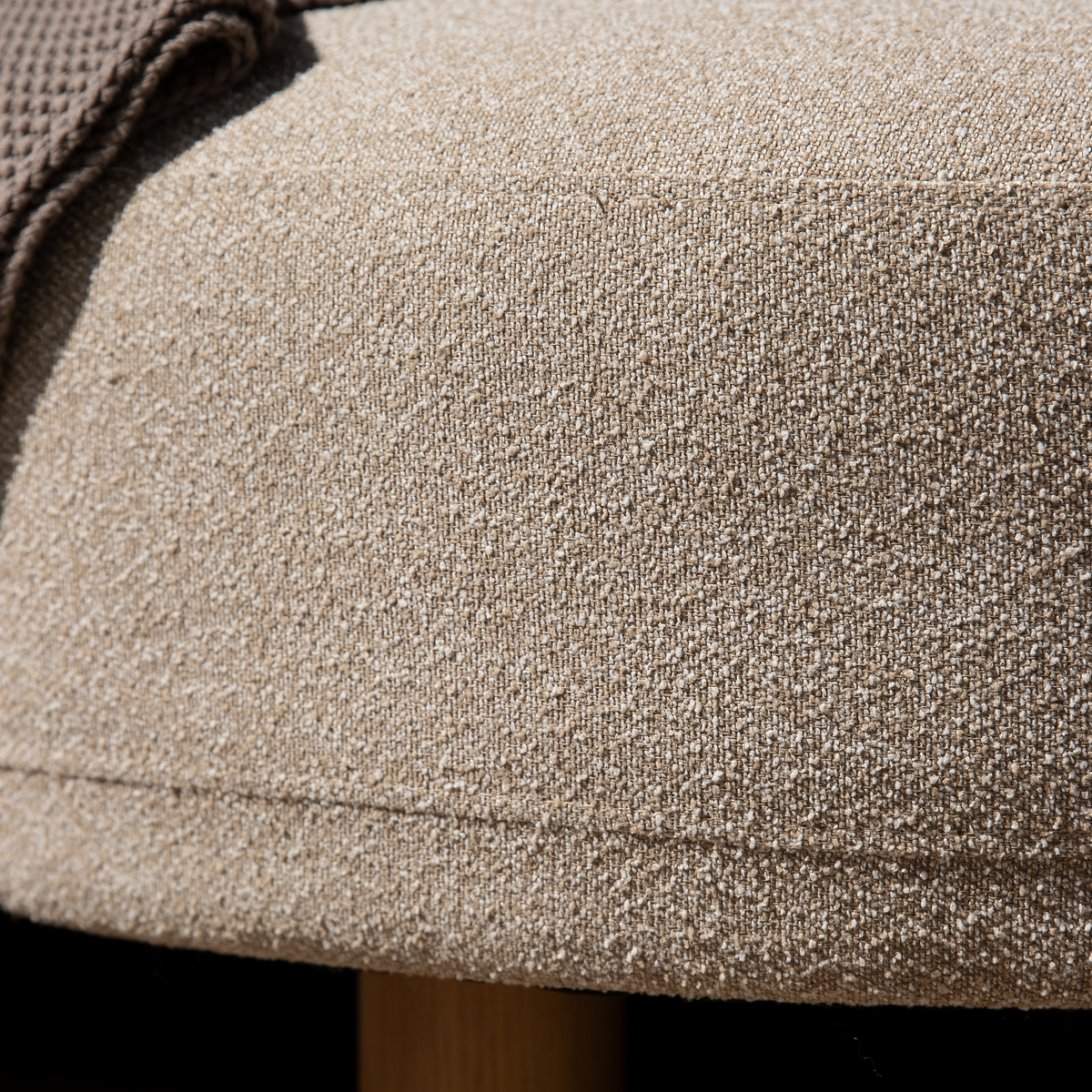 Nærbillede af beige bouclé-polstret pouf med træben og en strikket plaid i hjørnet.