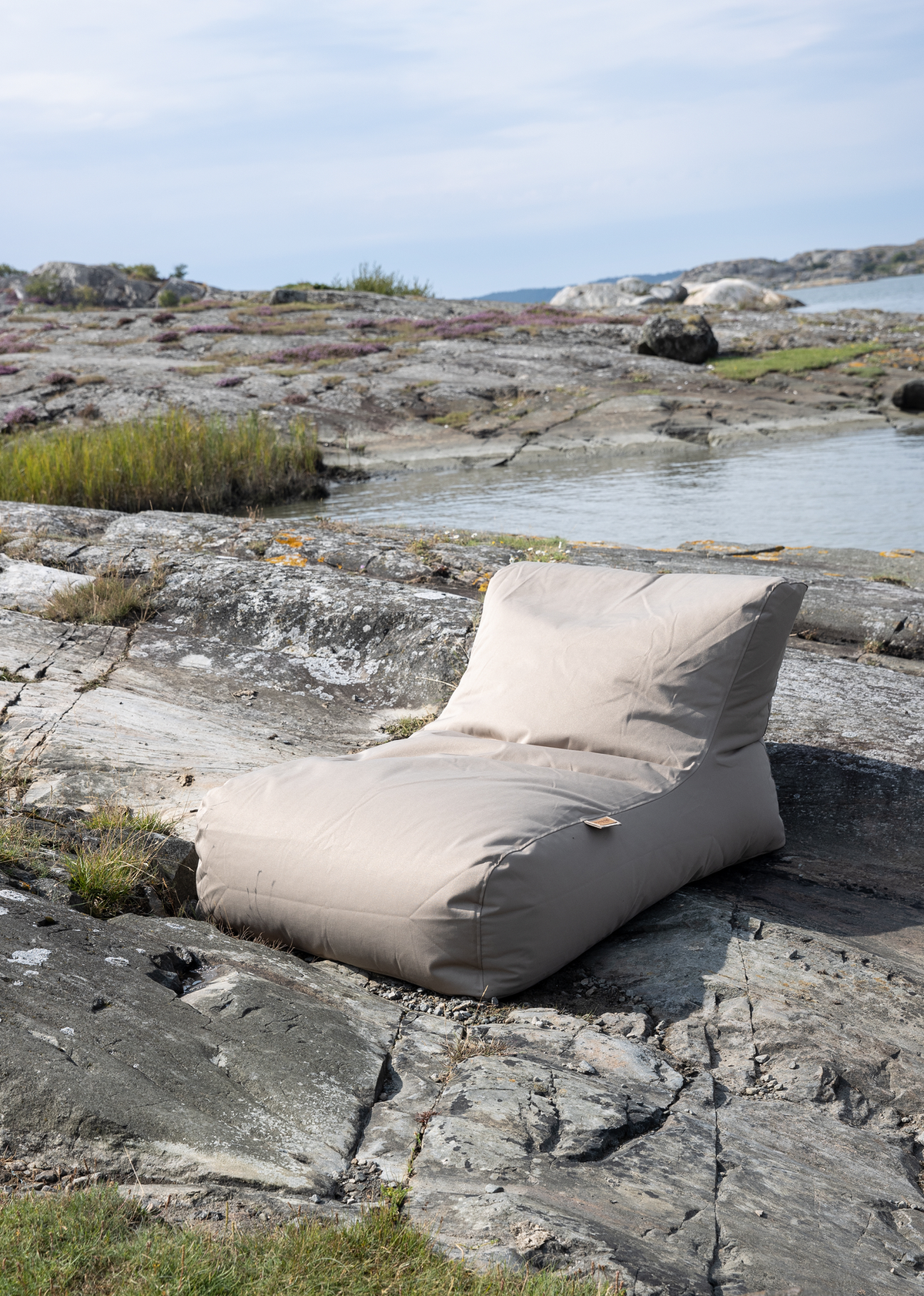 Beige loungemøbel i sækkestolsstil placeret på klippe ved kysten i dagslys.