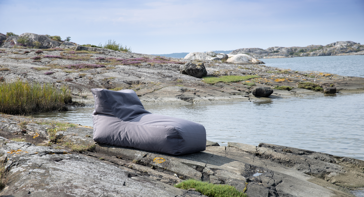 Grå sækkestol/liggestol på klipper ved vandet under klar himmel.