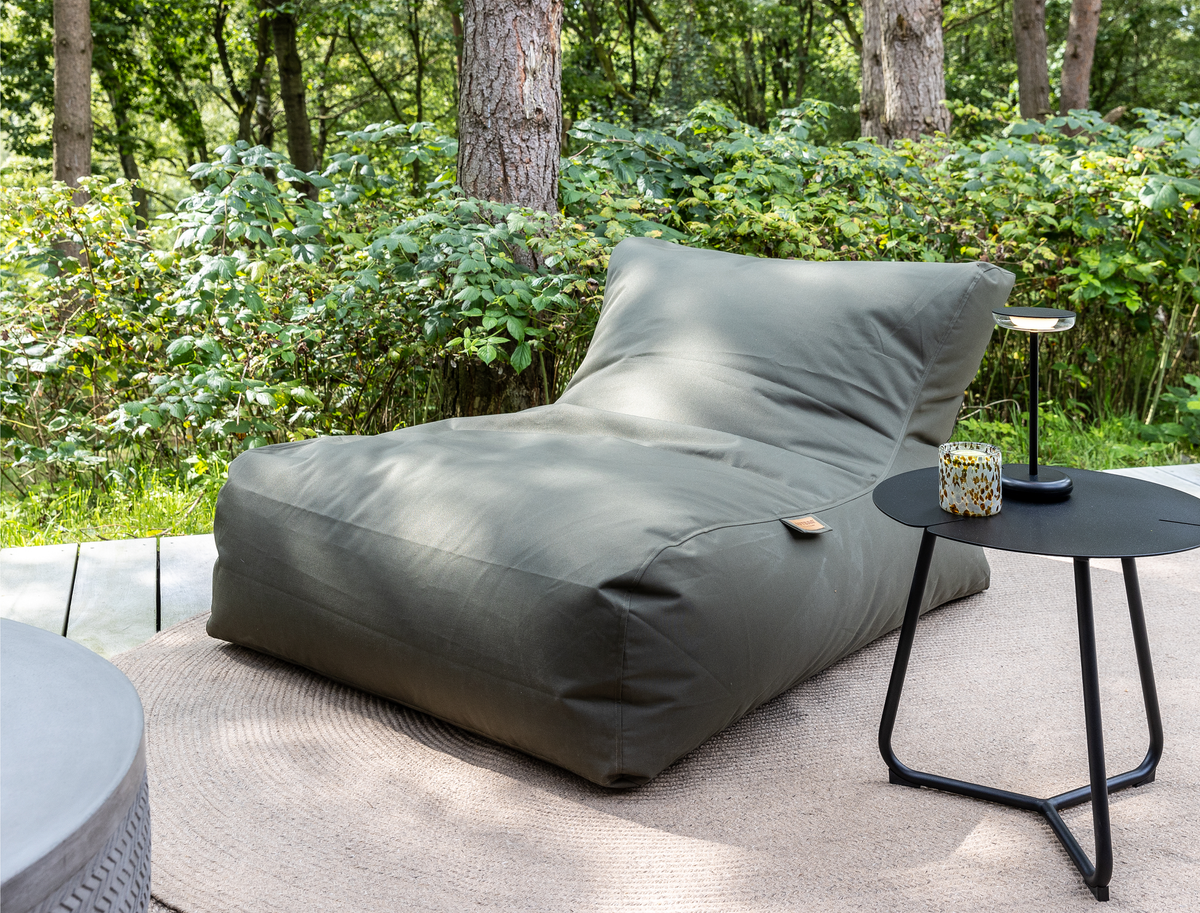 Grøn loungemøbel/beanbag på beige tæppe på terrasse i haven, med sort sidebord med bærbar lampe og lys, i dagslys.