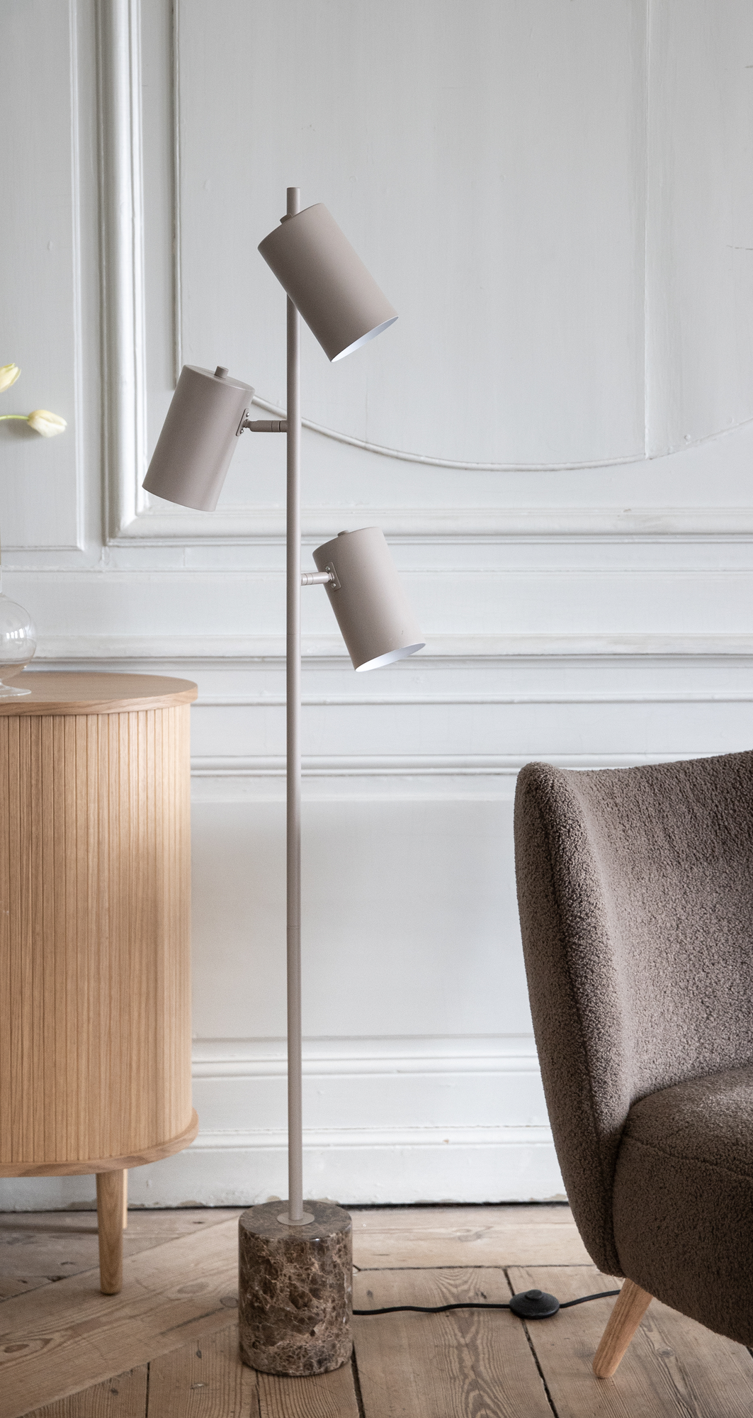 Beige gulvlampe med tre justerbare skærme og marmorfod ved siden af et træskab og en boucléstol i en lys stue.