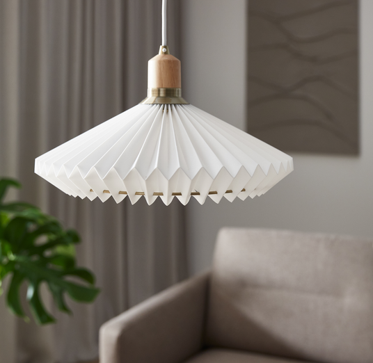 Hvid plisseret loftpendel med træ- og messingdetalje i en lys stue med beige sofa.