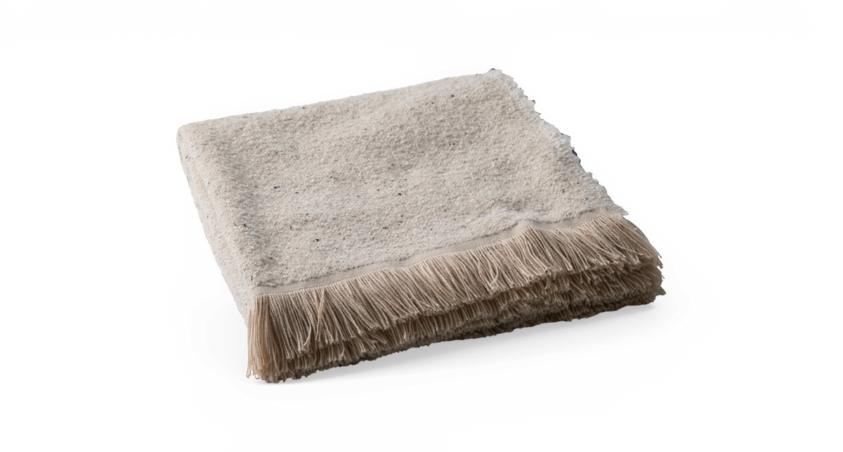 Beigefarvet plaid med frynset kant, sammenfoldet mod sort baggrund.