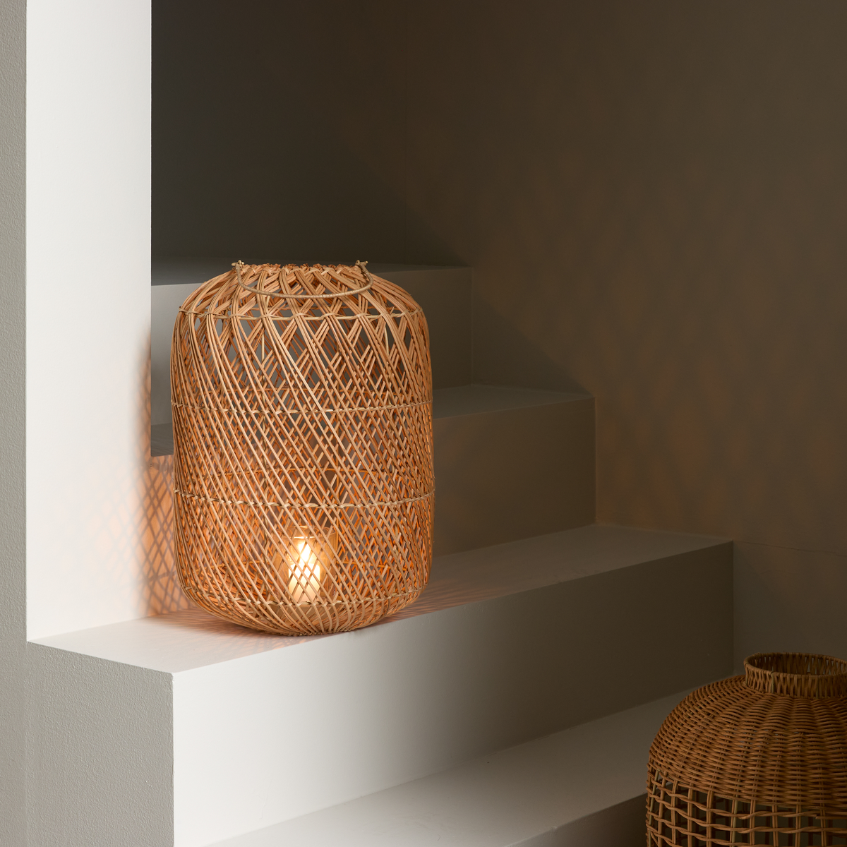 Flettet rattanlampe på hvide trin, der kaster et diamantformet skyggemønster.