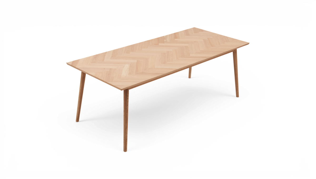 Rektangulært spisebord i lys eg med sildebensmønstret bordplade og slanke, tilspidsede ben på hvid baggrund.
