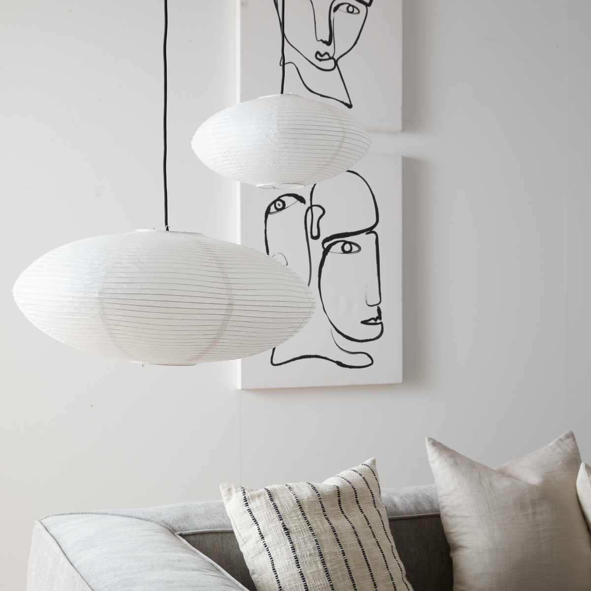 To hvide rispendler hænger over en grå sofa med neutrale puder; bagved ses to sort-hvide lineart-billeder med ansigter.