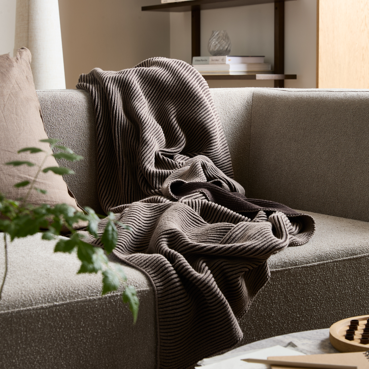 Beige sofa med rillet brun plaid og pude i et roligt stue-miljø.