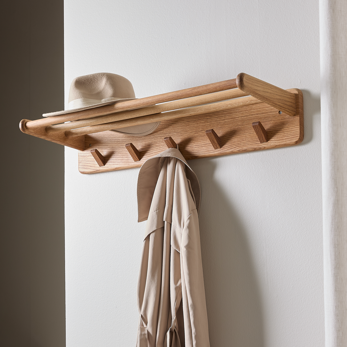 Vægmonteret knagerække i træ med hylde, beige hat ovenpå og beige frakke hænger.