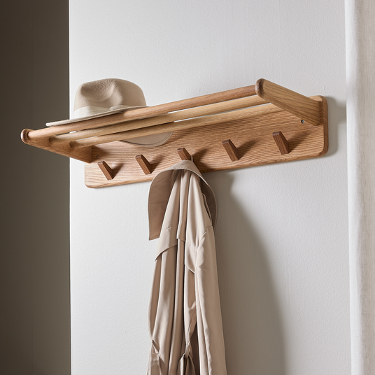 Vægmonteret knagerække i træ med hylde, beige hat ovenpå og beige frakke hænger.