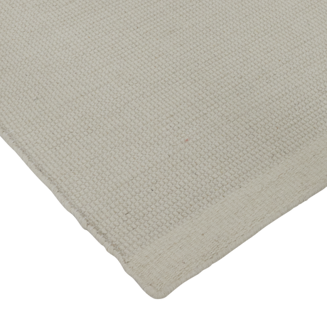 Nærbillede af lys beige vævet tæppe set fra hjørnet mod sort baggrund.
