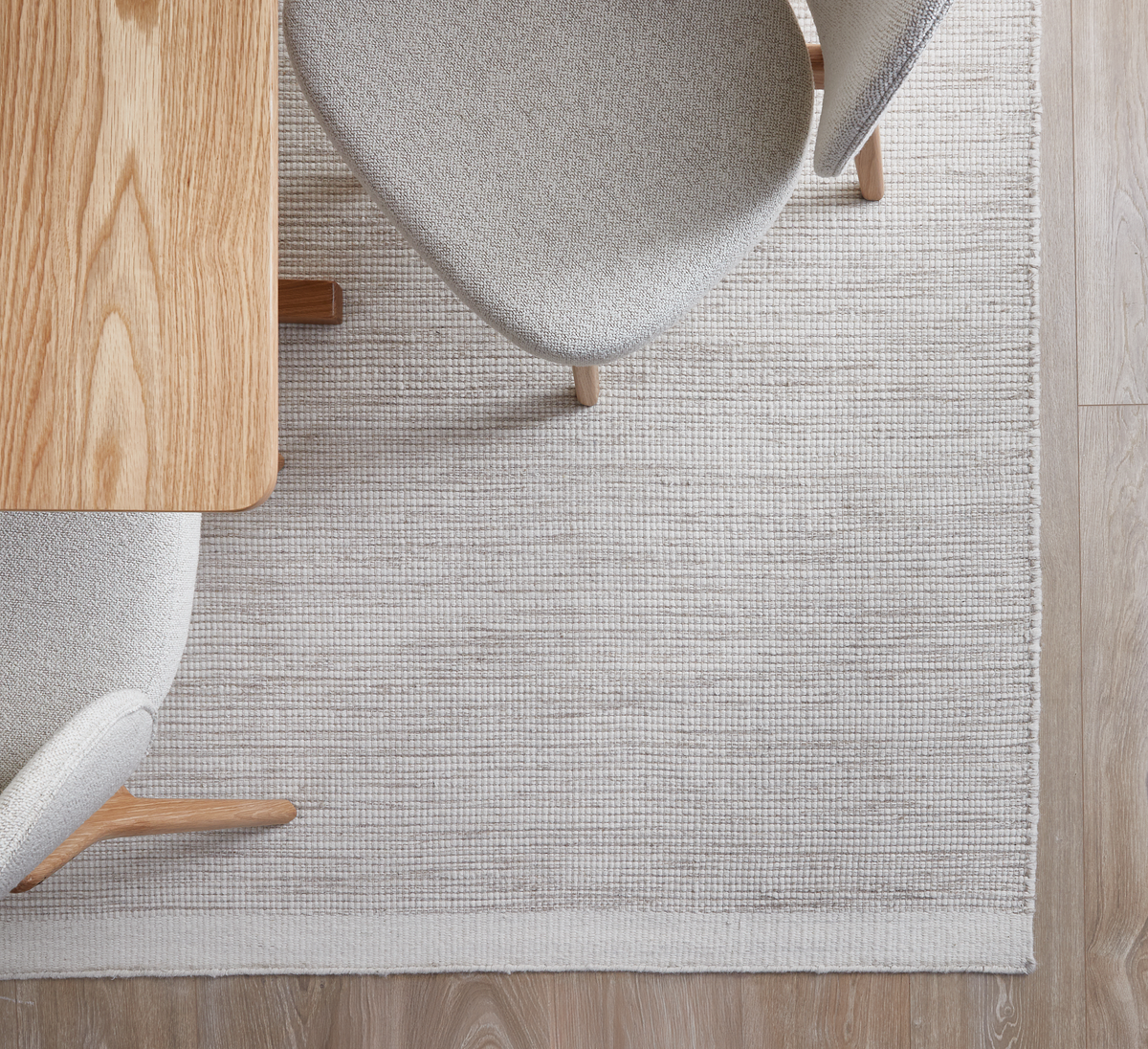 Lyst egetræsbord med to polstrede stole på et beige/hvidt vævet tæppe på trægulv, set oppefra.