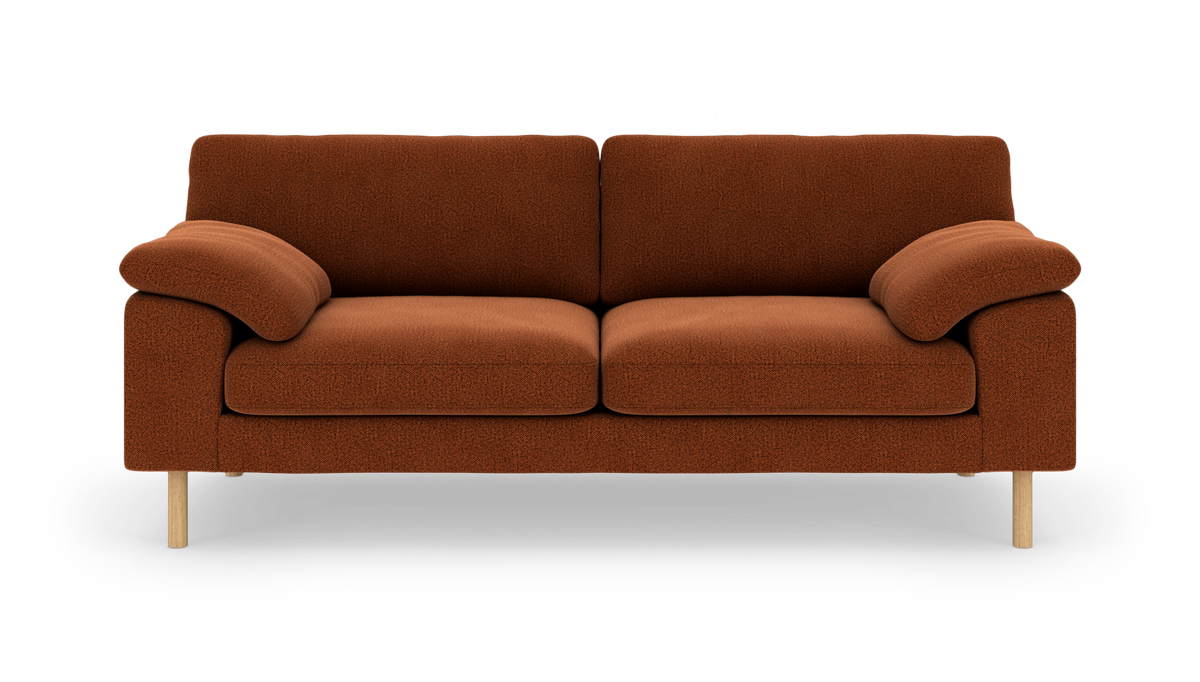 Rustrød sofa i tekstil med afrundede armlæn og lyse træben, fotograferet lige forfra på hvid baggrund.
