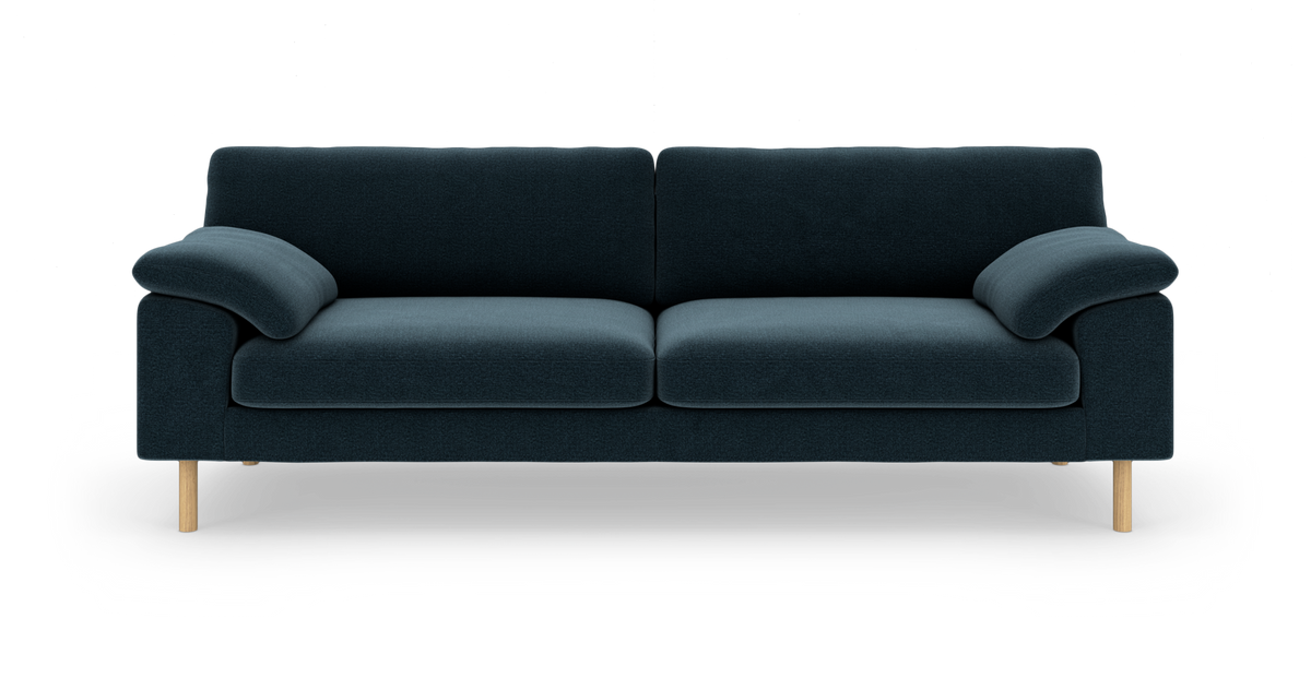Mørkeblå tresæders sofa med bløde armlæn og lyse træben, frontvisning på hvid baggrund.