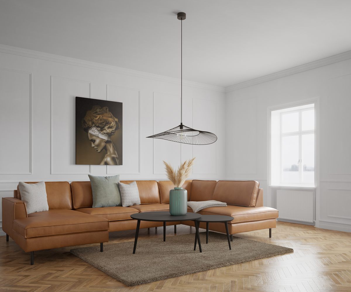 Lyst stue med brun lædersofa, sorte sofaborde, pampasgræs i grøn vase, moderne pendellampe og vægpaneler ved vindue i dagslys.