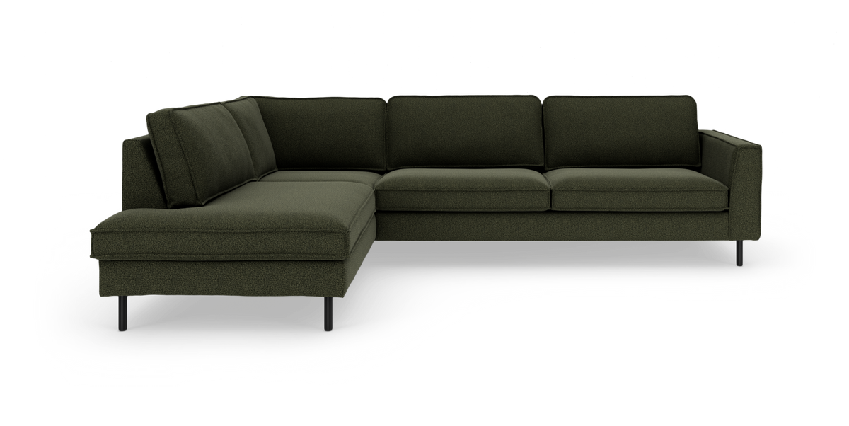 Mørkegrøn L‑sofa med chaiselong og slanke sorte ben, frilagt i studie.