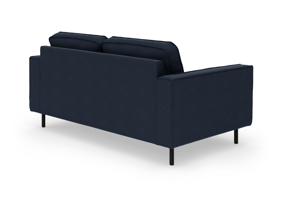 Mørkeblå sofa set skråt bagfra i studie, med slanke sorte ben på hvid baggrund.