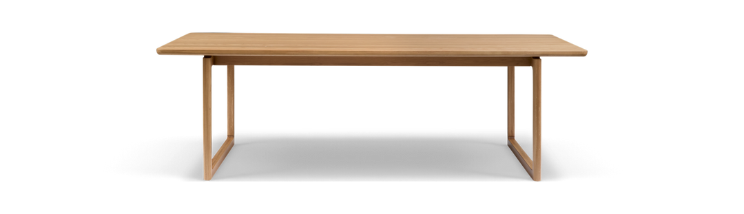 Rektangulært bord i lys eg med rammeformede ben, fritlagt på hvid baggrund.