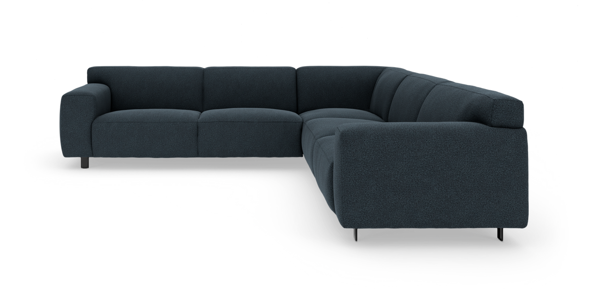 Mørkeblå L‑formet modulsofa i stof med afrundede puder og slanke metalben, fotograferet i trekvart vinkel.