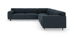 Mørkeblå L‑formet modulsofa i stof med afrundede puder og slanke metalben, fotograferet i trekvart vinkel.