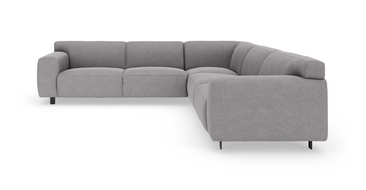 Lysegrå modulær hjørnesofa med brede armlæn og sorte metalben på frilagt hvid baggrund.