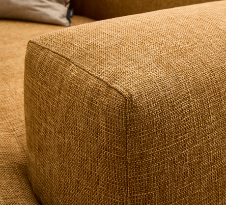 Nærbillede af sennepsgul vævet stofpolstring på sofaens armlæn med beige pude i baggrunden.