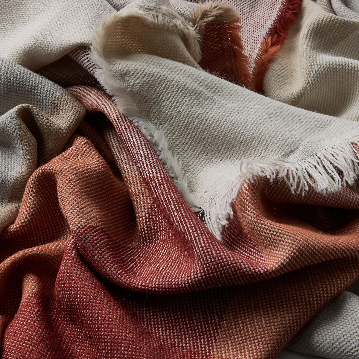 Nærbillede af vævet plaid med frynser i varme nuancer af rød, terrakotta og beige.