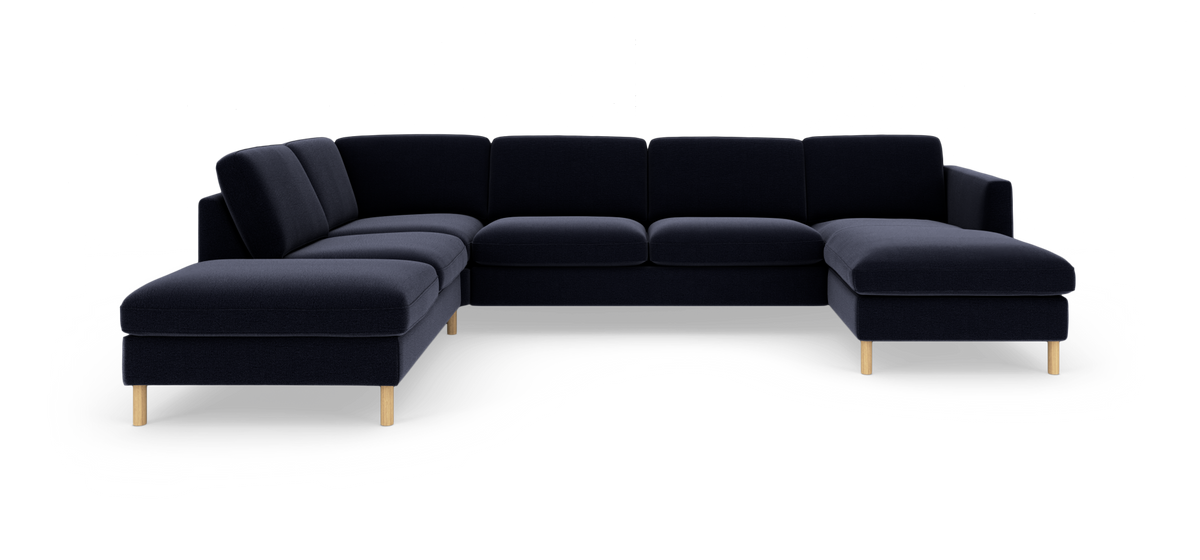 Mørk navyblå U-formet modulsofa med chaiselong i begge ender og lyse træben, fotograferet i studie.