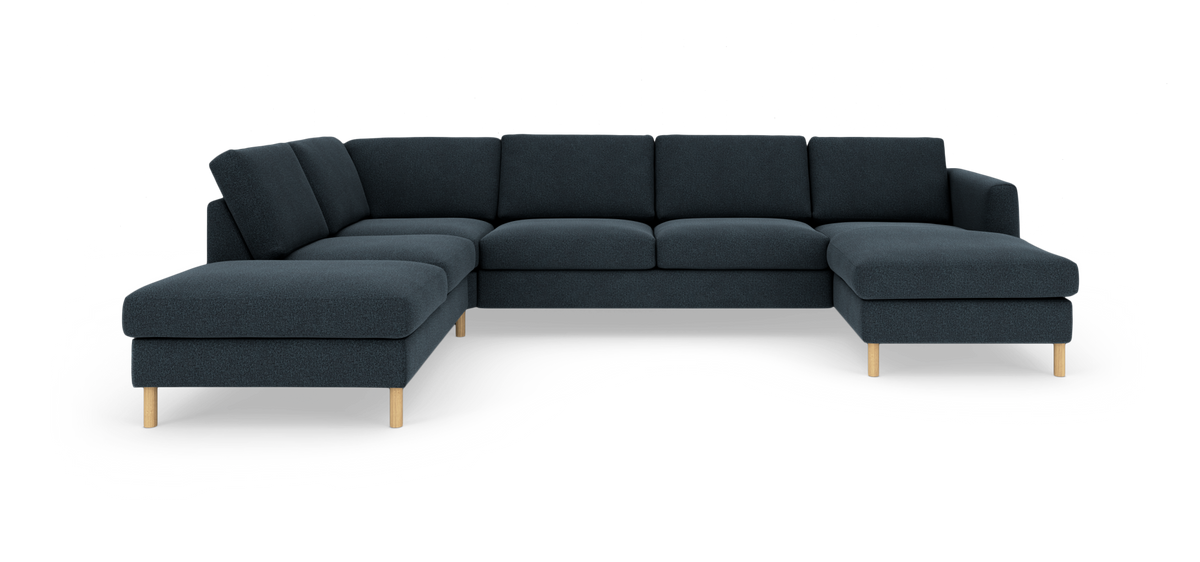Mørkeblå modulsofa i U‑form med chaiselong i begge ender og runde træben, frilagt mod hvid baggrund.