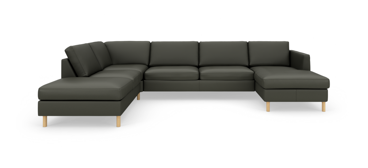 Modulsofa i mørkegrøn L‑form med chaiselong i begge ender og lyse træben, frilagt på hvid baggrund.