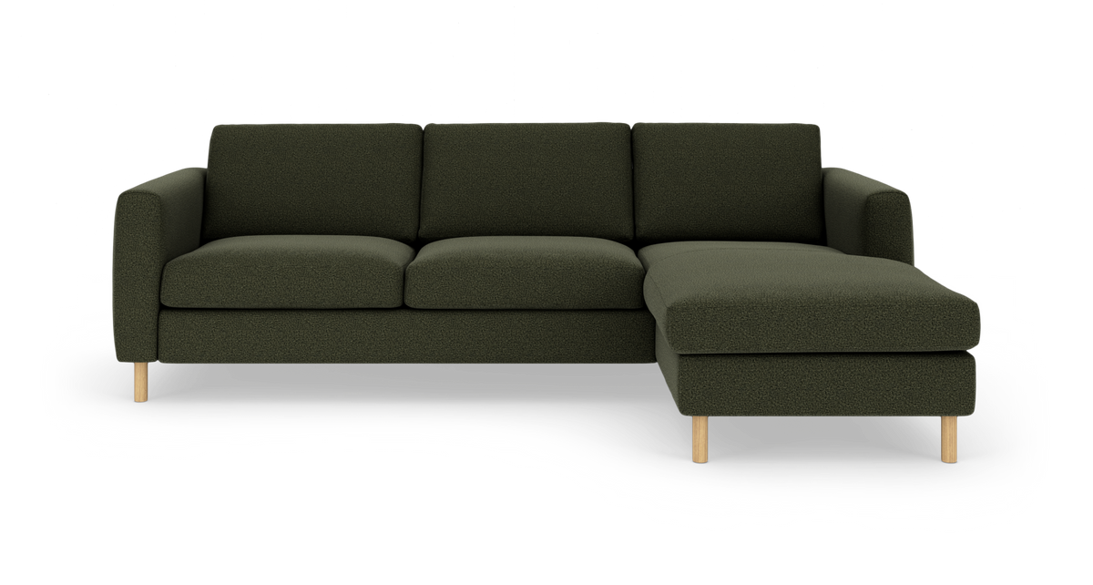 Mørkegrøn hjørnesofa med chaiselong til højre og lyse træben, fritlagt på hvid baggrund.