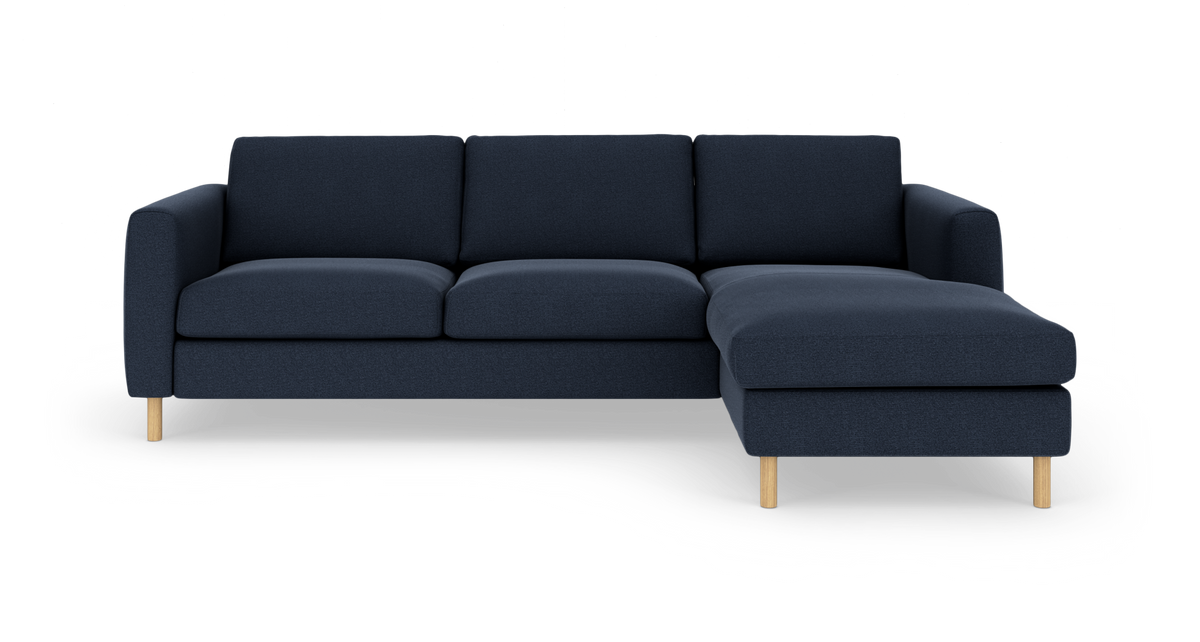 Mørkeblå hjørnesofa med chaiselong til højre og lyse træben, fritlagt på hvid baggrund.
