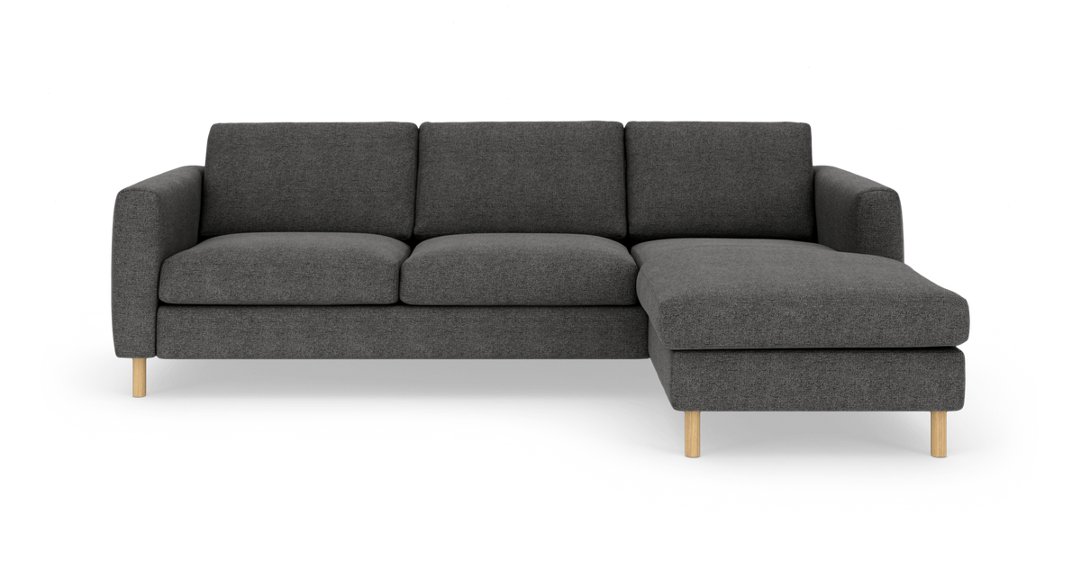 Mørkegrå hjørnesofa med chaiselong til højre og runde træben, frilagt på hvid baggrund.