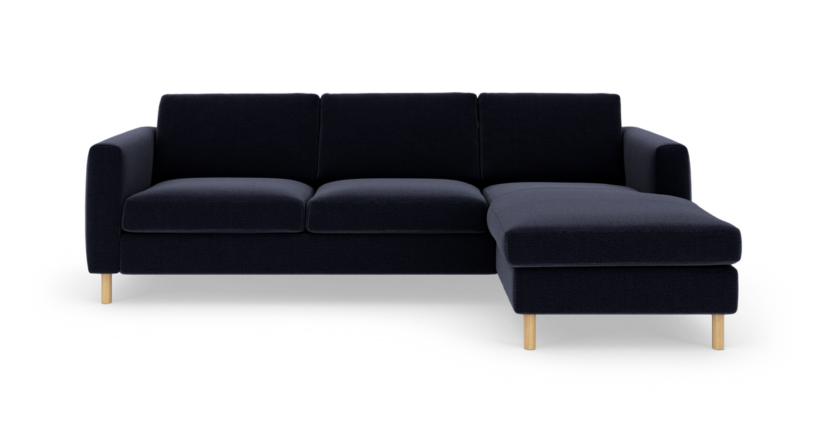 Mørkeblå modulsofa med chaiselong til højre og lyse træben, fotograferet forfra på studiobaggrund.