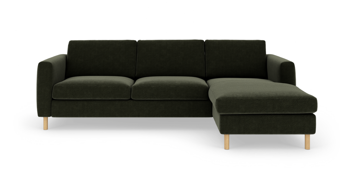 Mørkegrøn hjørnesofa med chaiselong til højre og lyse træben, fotograferet forfra.