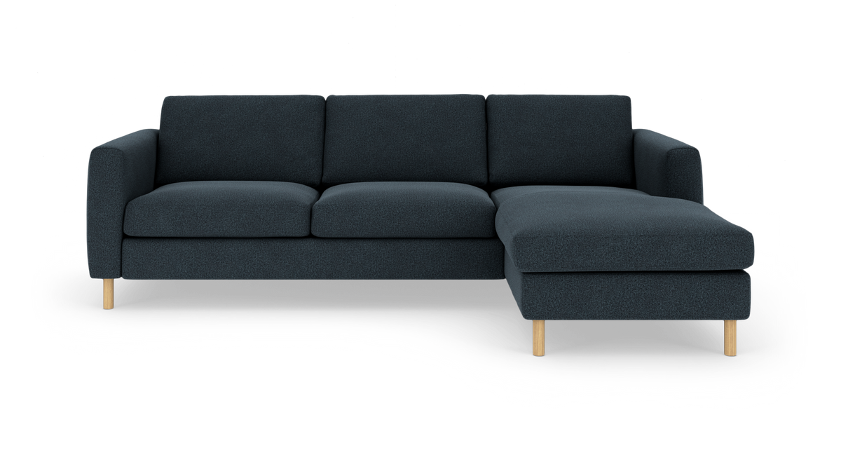 Mørkeblå hjørnesofa med chaiselong til højre og lyse træben, frilagt på hvid baggrund.