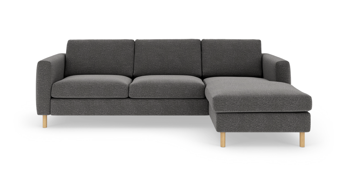 Mørkegrå sofa med chaiselong til højre og lyse træben, enkel moderne design, frilagt på hvid baggrund.