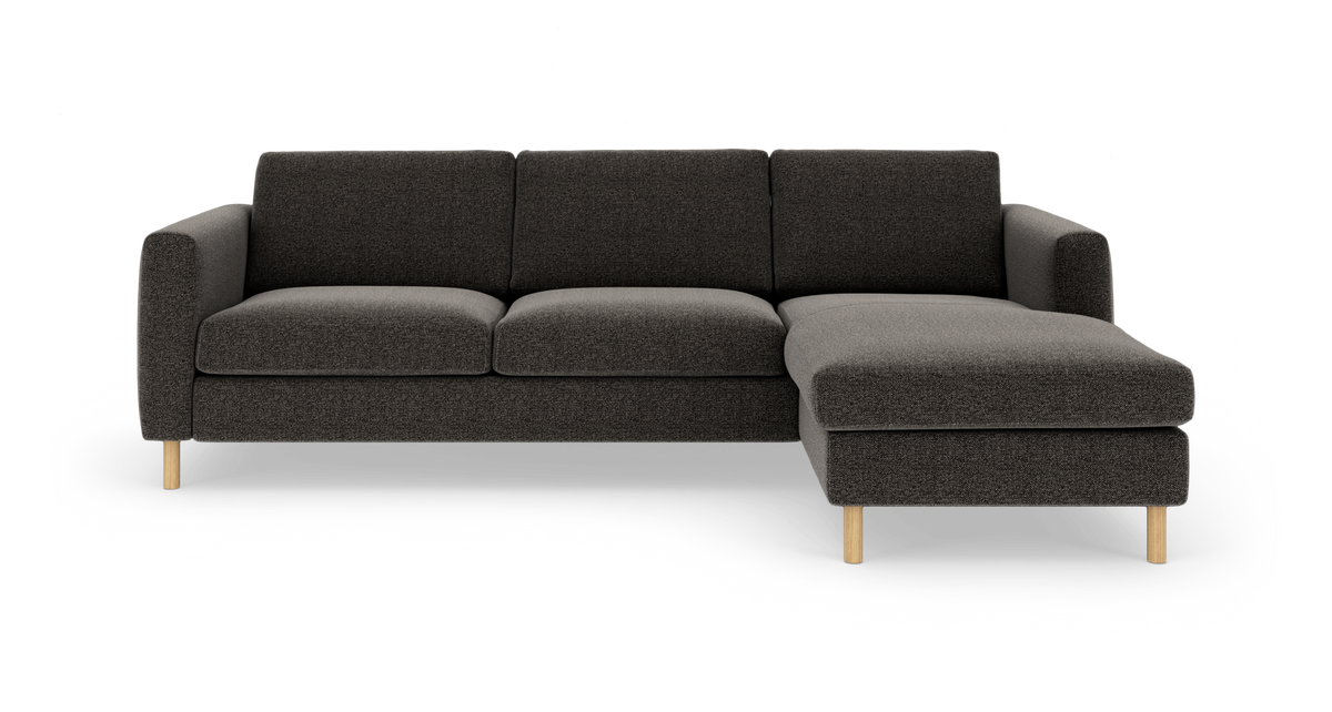 Mørkegrå hjørnesofa med chaiselong til højre og lyse træben, fritlagt på hvid baggrund.