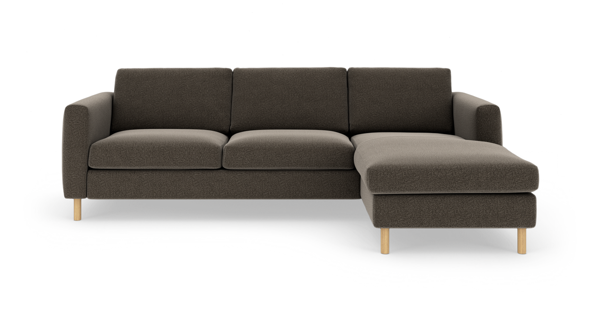 Mørkegrå hjørnesofa med chaiselong til højre og lyse træben, fritlagt på hvid baggrund.