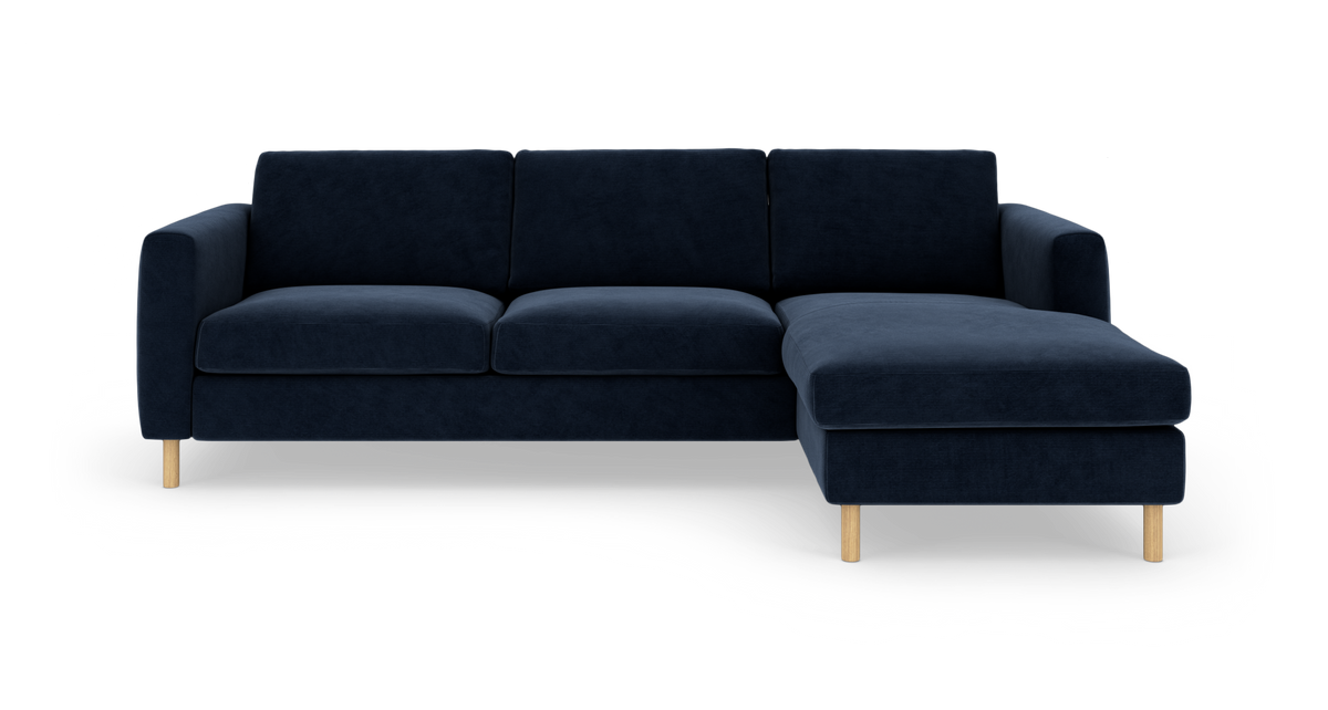 Mørkeblå hjørnesofa med chaiselong til højre og lyse træben, frilagt på hvid baggrund.